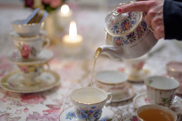 woman pouring tea into vintage tea cup on table inside for adult tea party